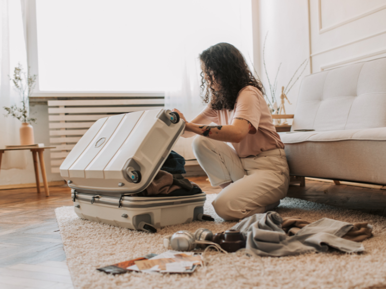 Woman kneeling on a rug packing clothes into an open hard-shell suitcase
