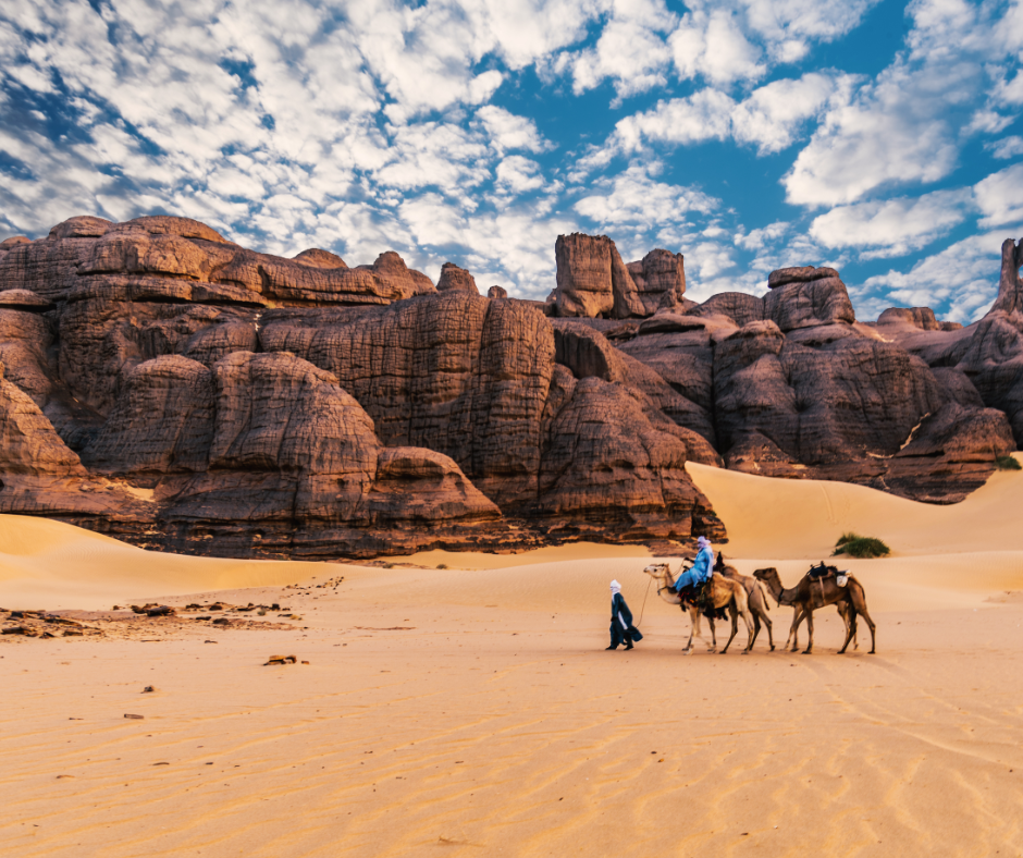 Tuareg guide leading camels past sandstone formations near Djanet in the Tassili