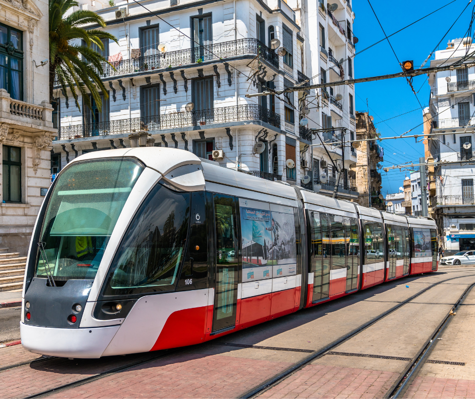Modern red and white tram passing colonial apartment buildings in an Algerian city street