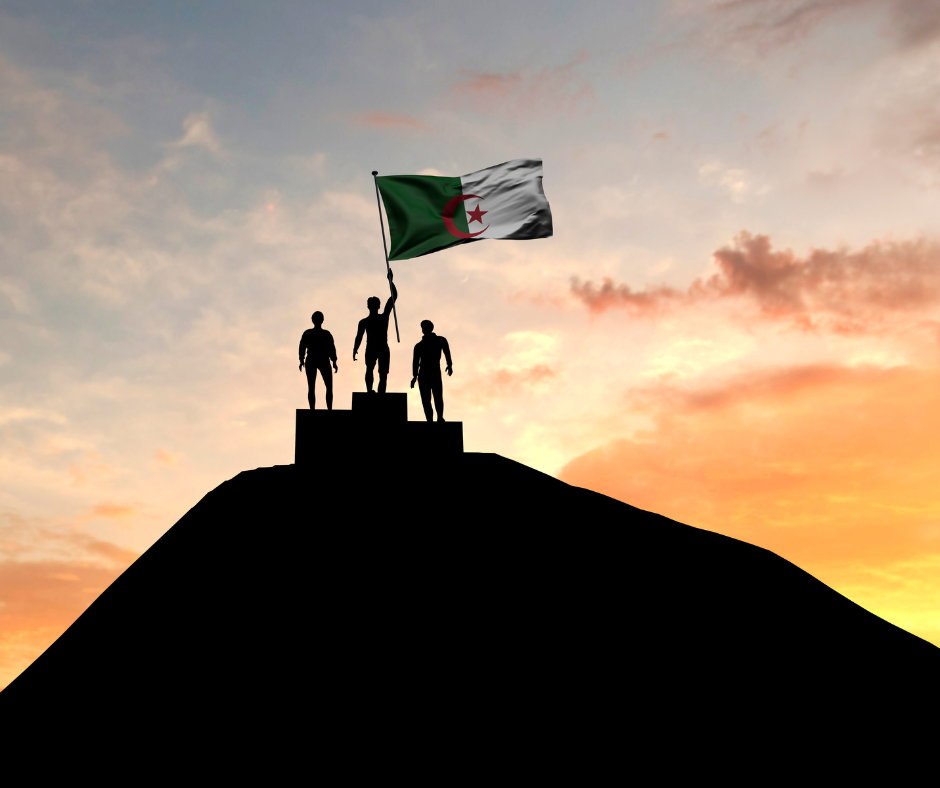 Silhouettes of three people on a hilltop podium raising the Algerian flag at sunset