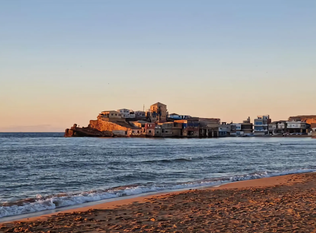 Sandy beach at sunset with seaside houses on a rocky point, El Oued Halouf
