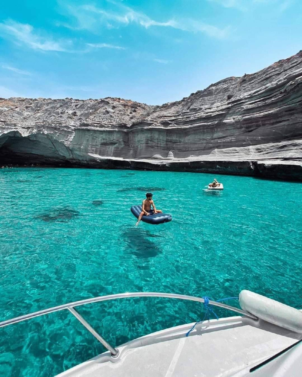 Swimmer on an inflatable in turquoise water beneath layered white cliffs at La Guitare, M'Said