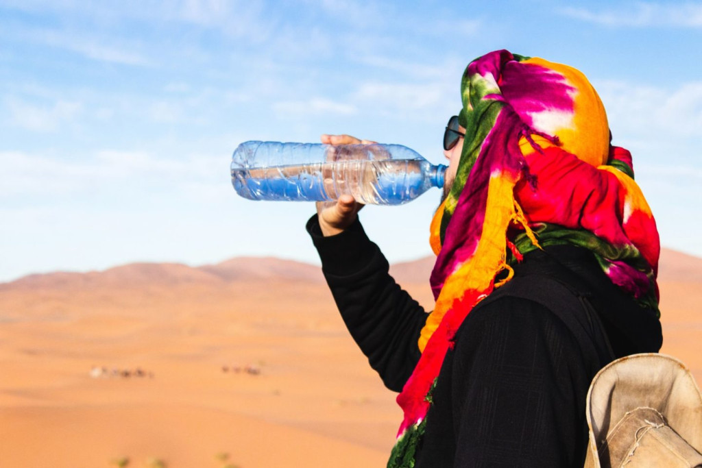 Traveler in a colorful headscarf drinking bottled water in front of Sahara sand dunes