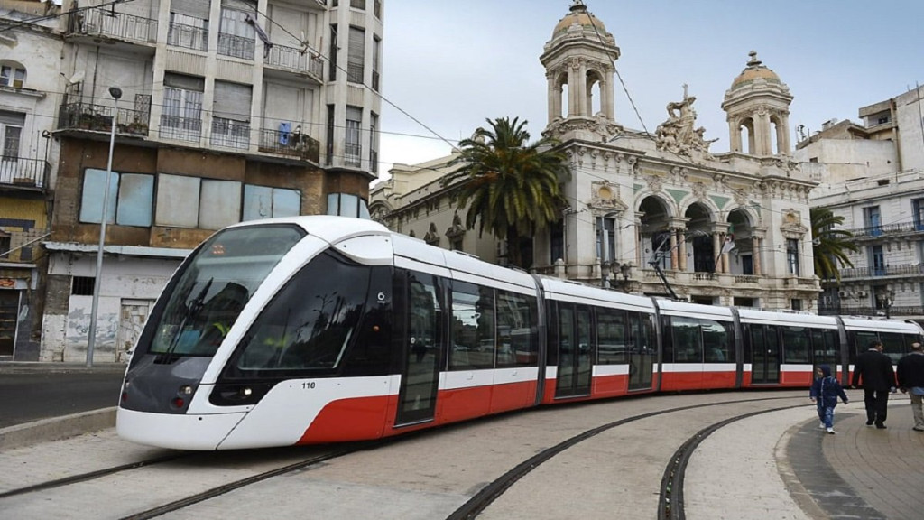 Red and white tram on a curving track in front of an ornate theater