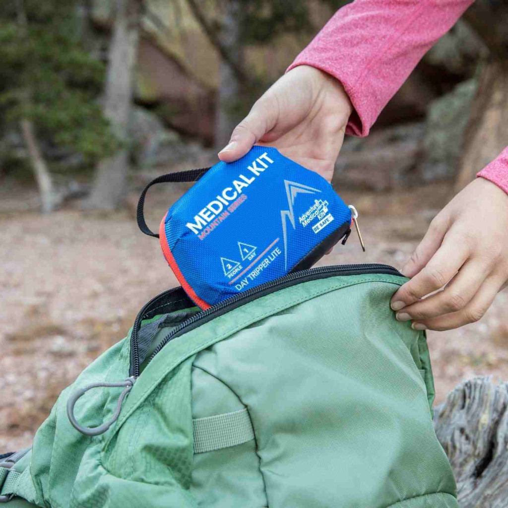 Traveler slipping a compact first aid kit into a green backpack
