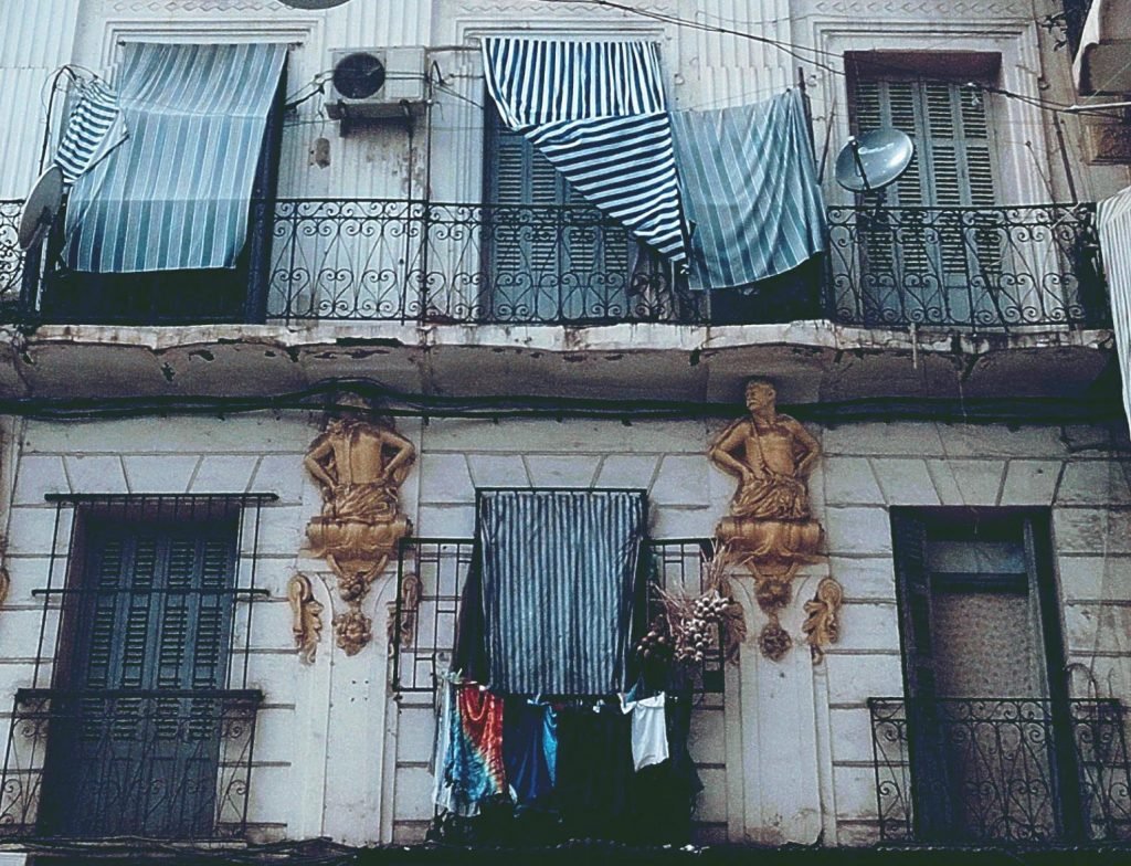 Old Bab El Oued building with sculpted figures, iron balconies and laundry hanging out