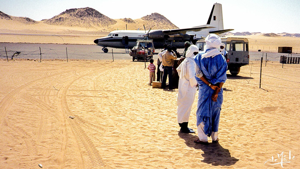 Tuareg men in robes waiting beside a propeller plane on a sandy Saharan airstrip