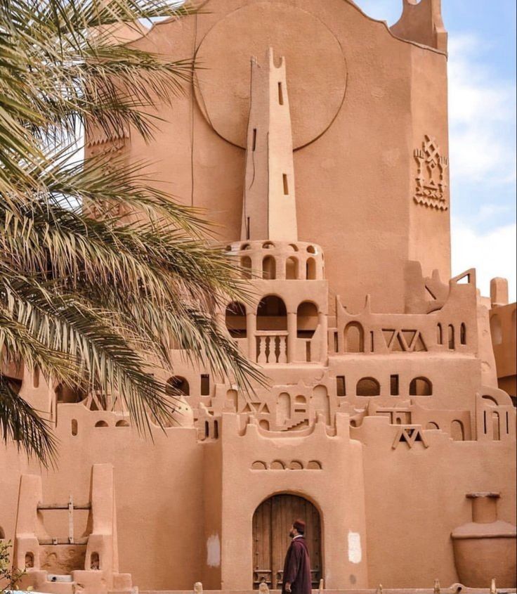 Red earthen Sudanese-style facade with palm fronds, typical of Timimoun