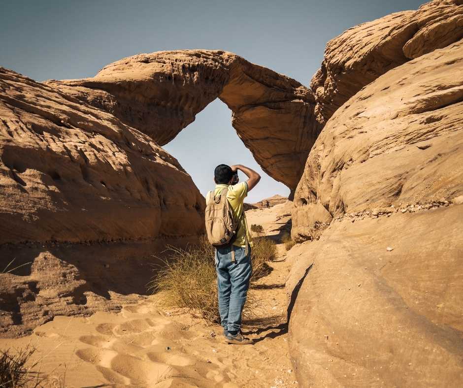backside of a young person taking a picture of rock formation at al Alula, Saudi Arabia