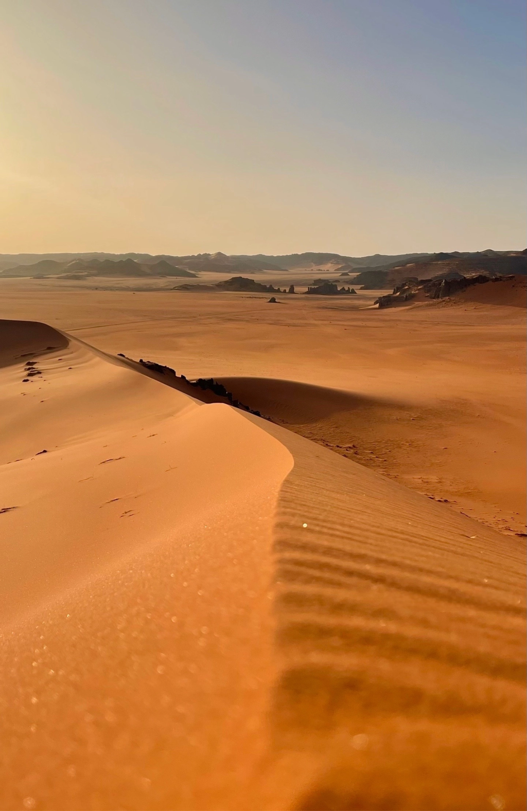Sand dune ridge with rippled slope and rocky hills in the distance at golden hour