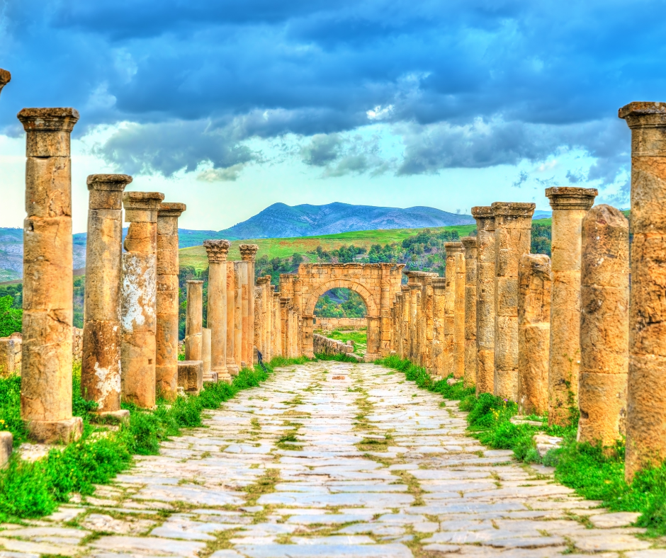 Paved Roman street lined with columns leading to an arch at Djemila