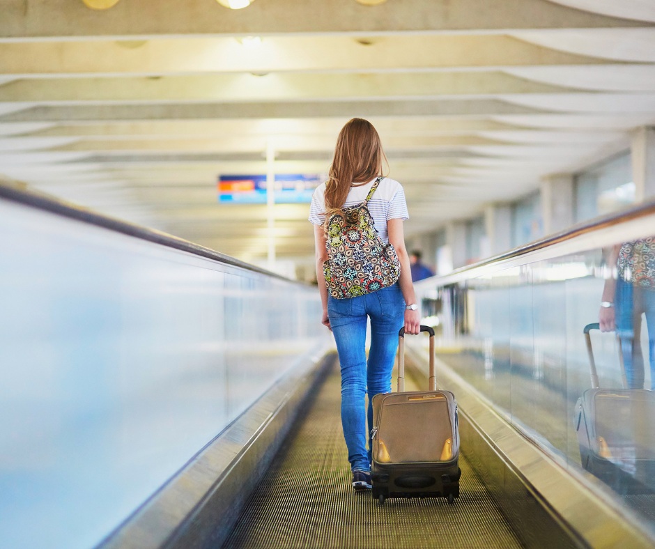 Young traveler with a backpack and rolling suitcase walking along an airport moving walkway