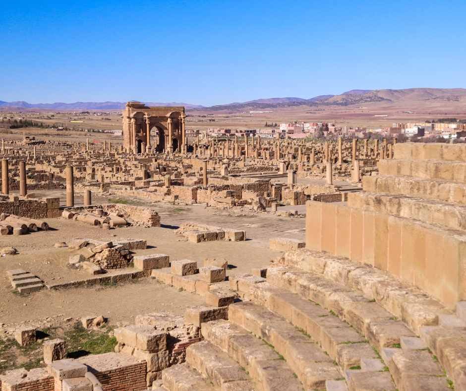 Ruins of Timgad with columns, a distant arch and stone theater steps in the foreground