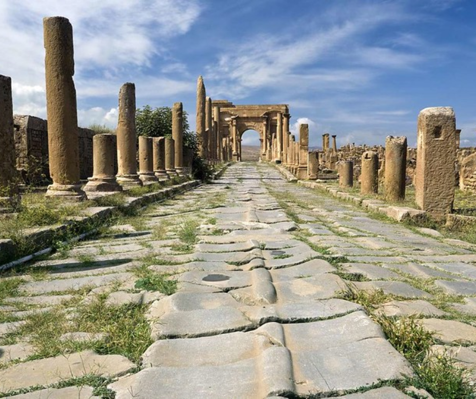 Paved Roman road lined with columns leading to an arch at Timgad
