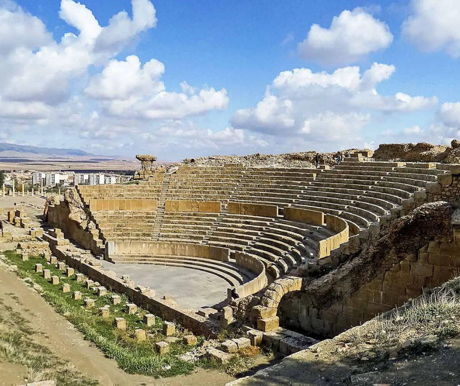 Semicircular stone seating of the Roman theater at Timgad under a cloudy blue sky