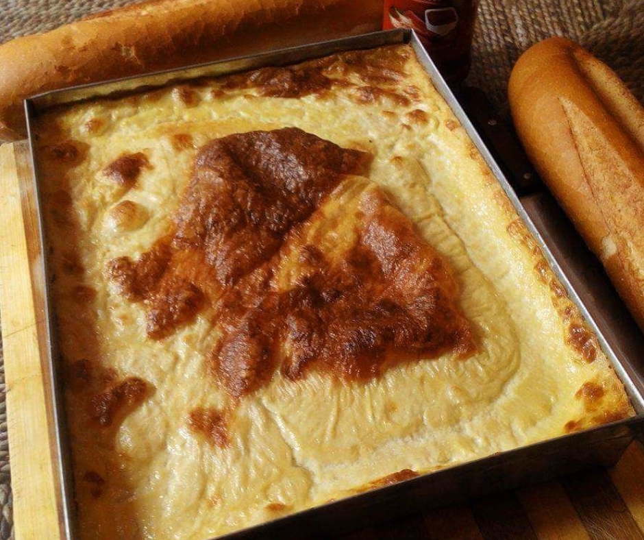 Baked karantika chickpea flan in a metal tray beside two baguettes