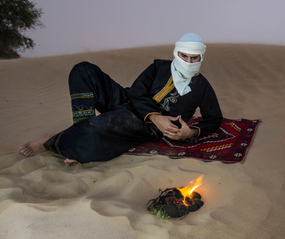 Man in a white veil reclining on a rug beside a small fire