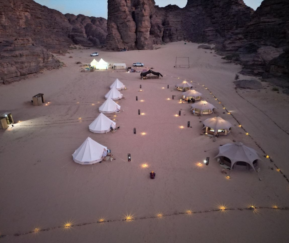 Aerial view of white bell tents and lanterns at dusk below red cliffs