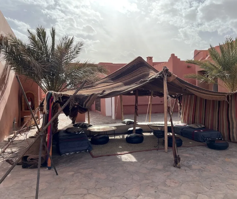 Bedouin-style striped tent with floor cushions in a pink adobe courtyard with palm trees