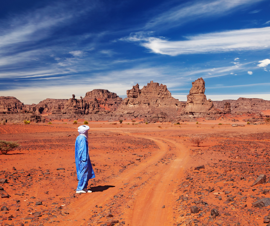 Tuareg guide in a blue robe standing on a desert track toward rock formations