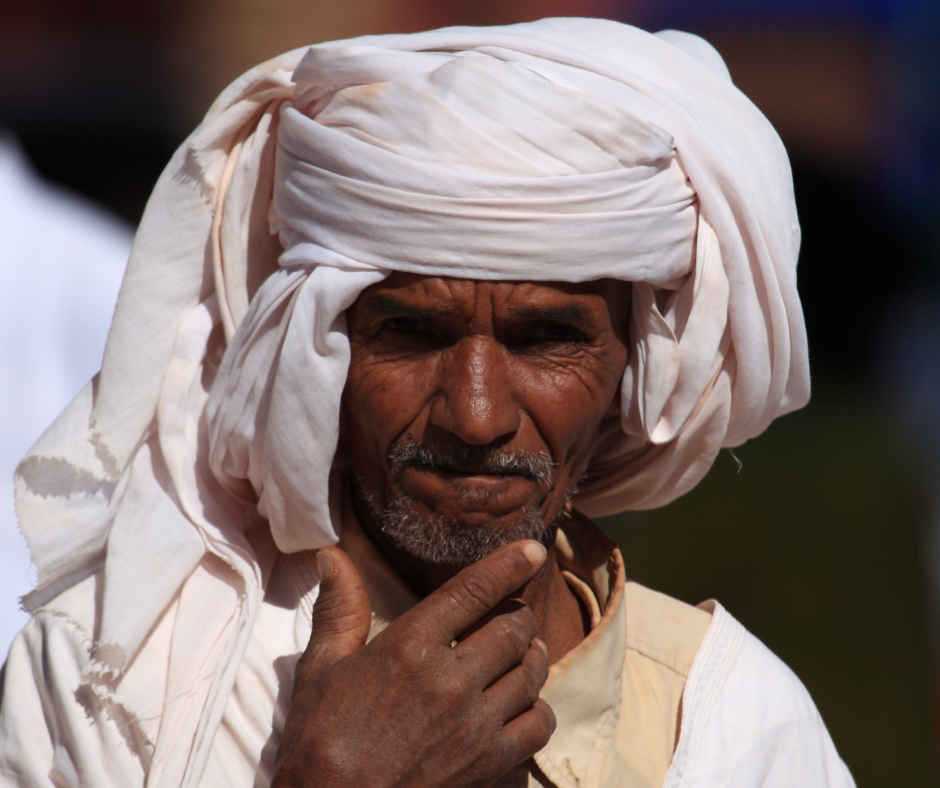 Close-up portrait of an older man in a white turban with his hand at his chin