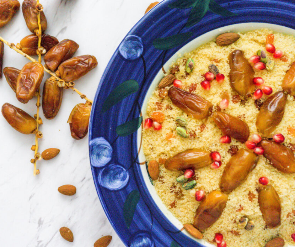 Sweet couscous mesfouf topped with dates, pomegranate seeds and almonds in a blue bowl