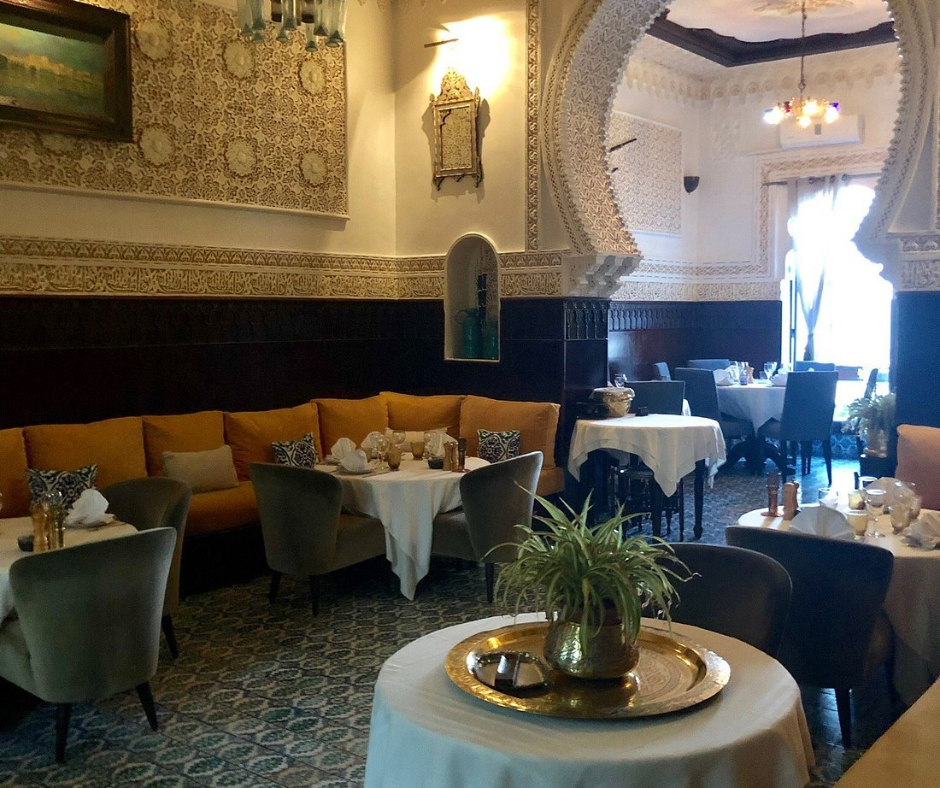 Elegant Algiers restaurant dining room with white tablecloths, carved plaster arches and orange banquettes