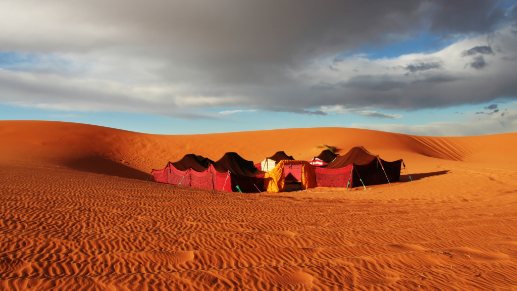 Red and black tents of a desert camp among orange dunes