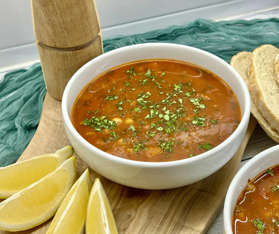 Bowl of Algerian chorba soup topped with parsley, served with lemon wedges and bread