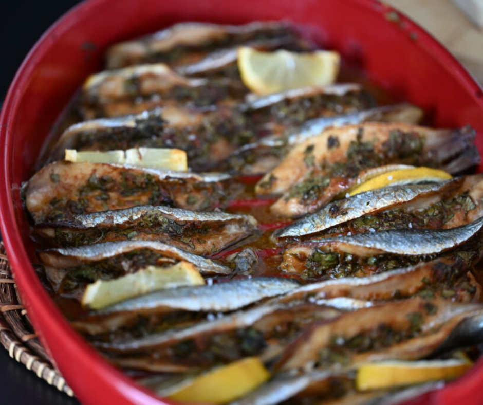 Baked sardines with herbs and lemon slices in a red dish