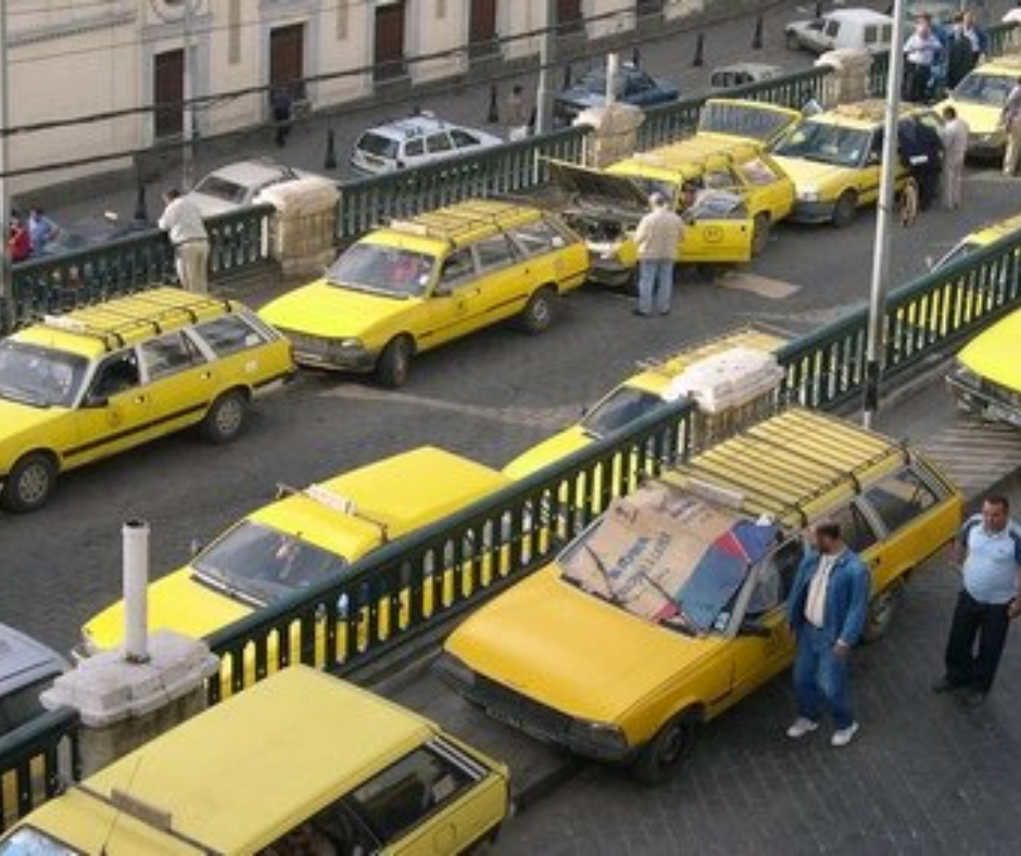 Row of yellow taxis parked along a green railing in an Algerian city