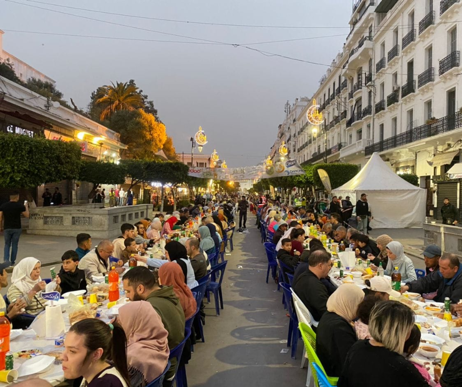 Long communal iftar table filling a lit Algerian city street at dusk