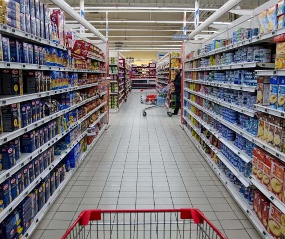 Supermarket aisle lined with packaged food and an empty red shopping cart