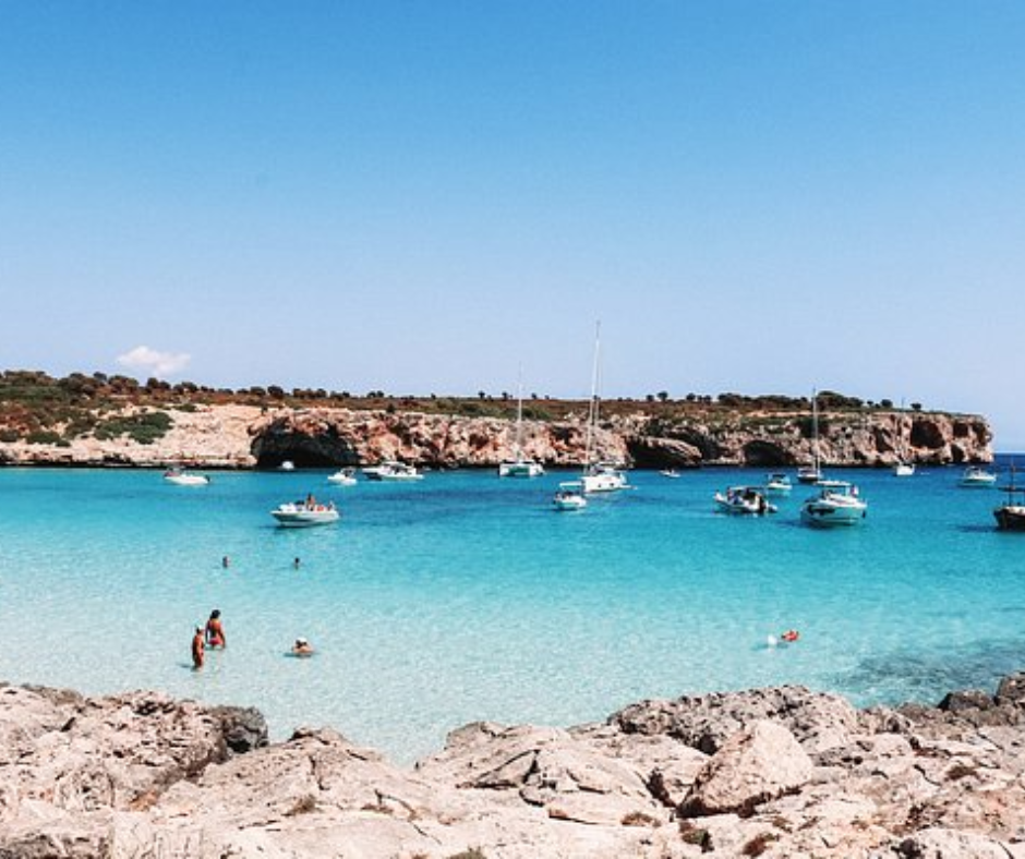 Turquoise cove with anchored boats and swimmers beside rocky shore