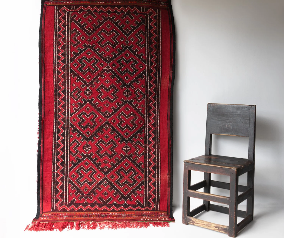 Red and black hand-woven rug with cross motifs hanging beside a wooden chair