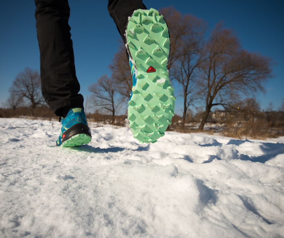 Sole of a green trail running shoe stepping through fresh snow