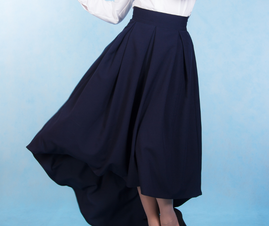 Woman twirling in a long navy skirt and white blouse on a blue backdrop
