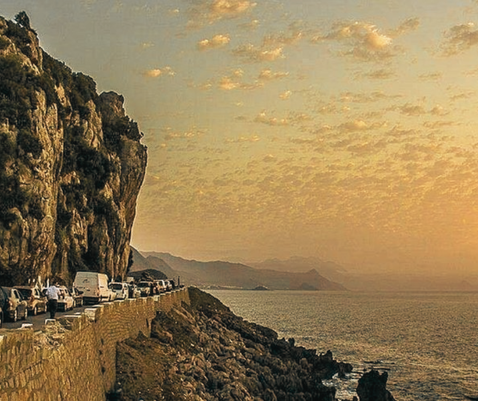 Coastal road along a cliff at sunset with parked cars, near Jijel