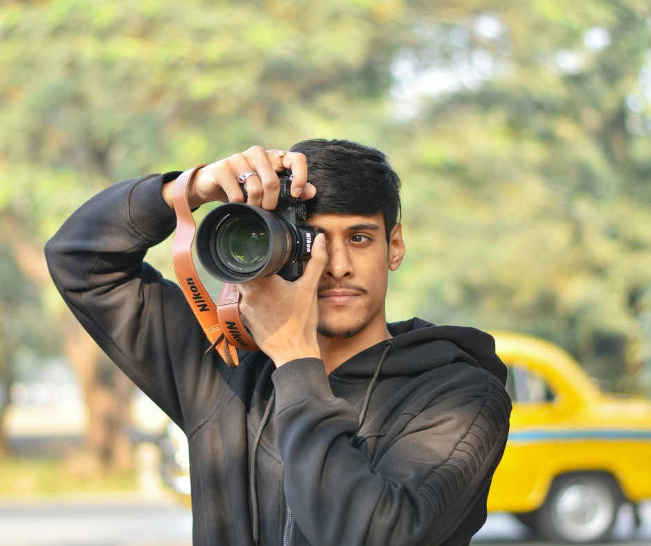 Man aiming a Nikon camera, with a yellow taxi behind him