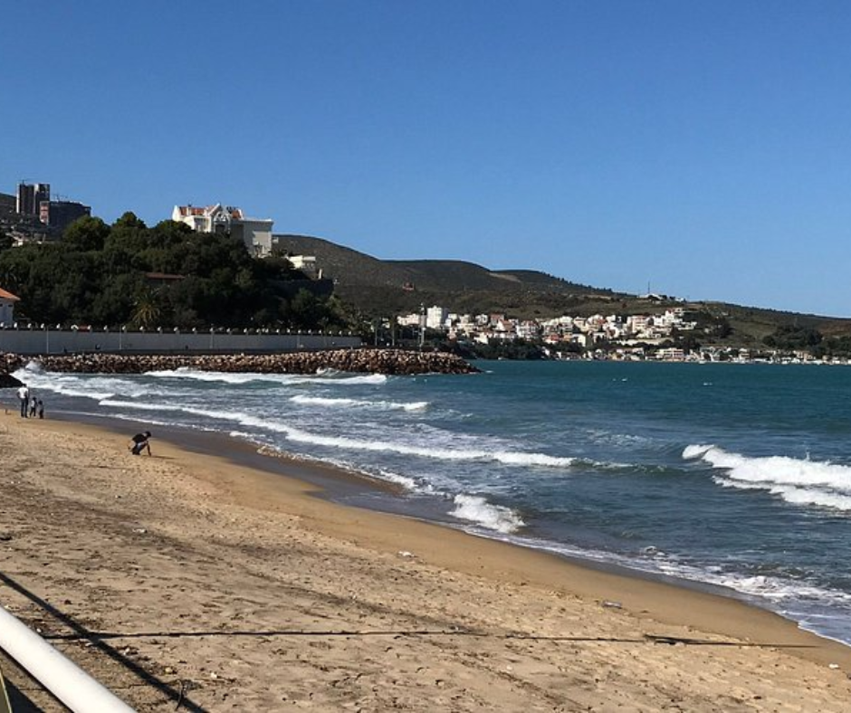 Waves on a sandy beach with the Annaba coastline in the distance