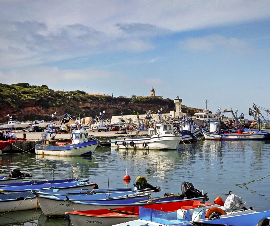 Fishing boats moored in the small harbor at Tipaza with lighthouse behind