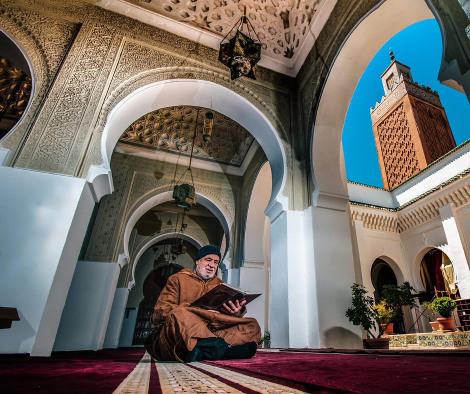Man reading inside the Sidi Boumediene mosque complex in Tlemcen, with a brick minaret behind