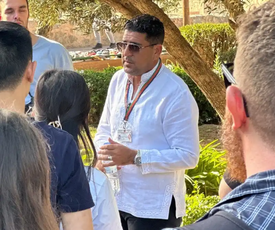 Guide with sunglasses and a lanyard talking to a small tour group outdoors