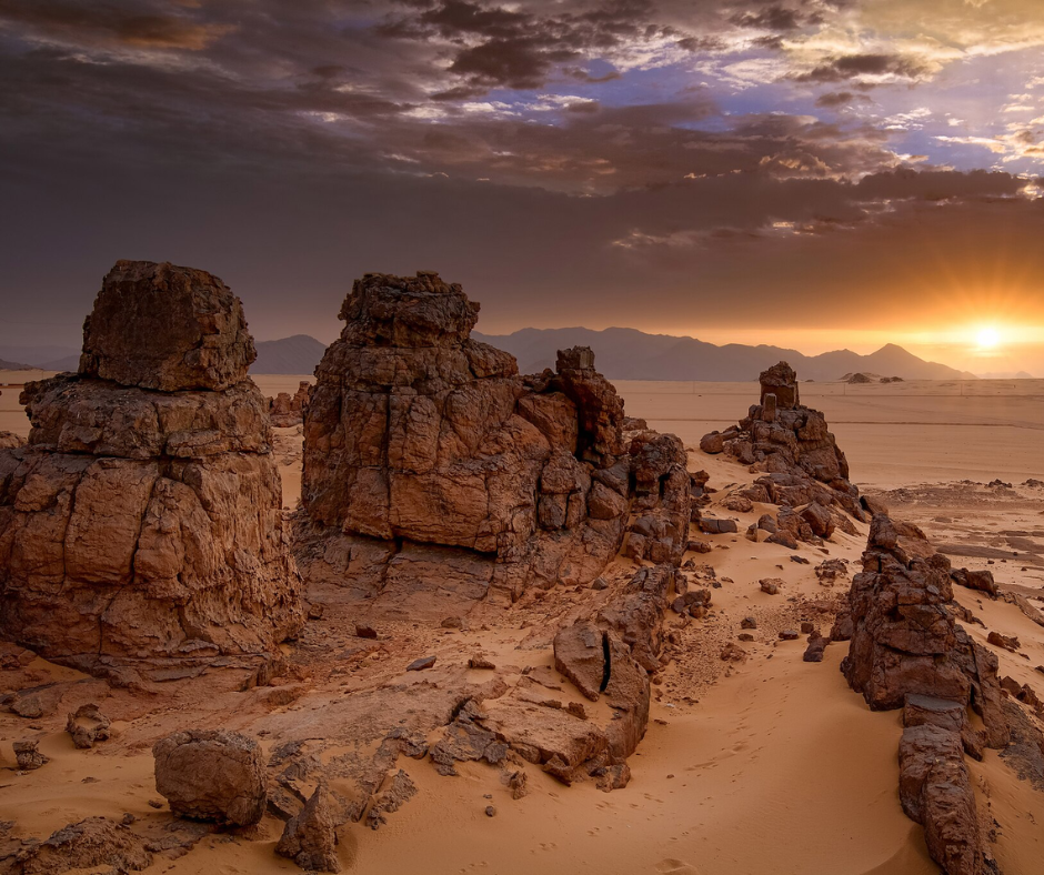 Eroded sandstone pillars on a sandy plain at sunset in the Tassili n'Ajjer