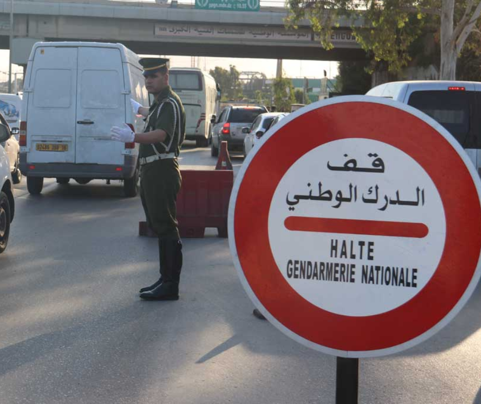 Gendarmerie officer waving traffic past a checkpoint sign in Algeria