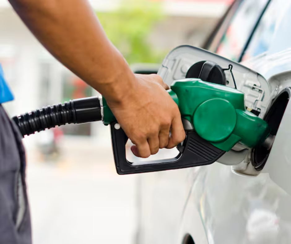 Hand holding a green fuel nozzle filling a car at a gas station
