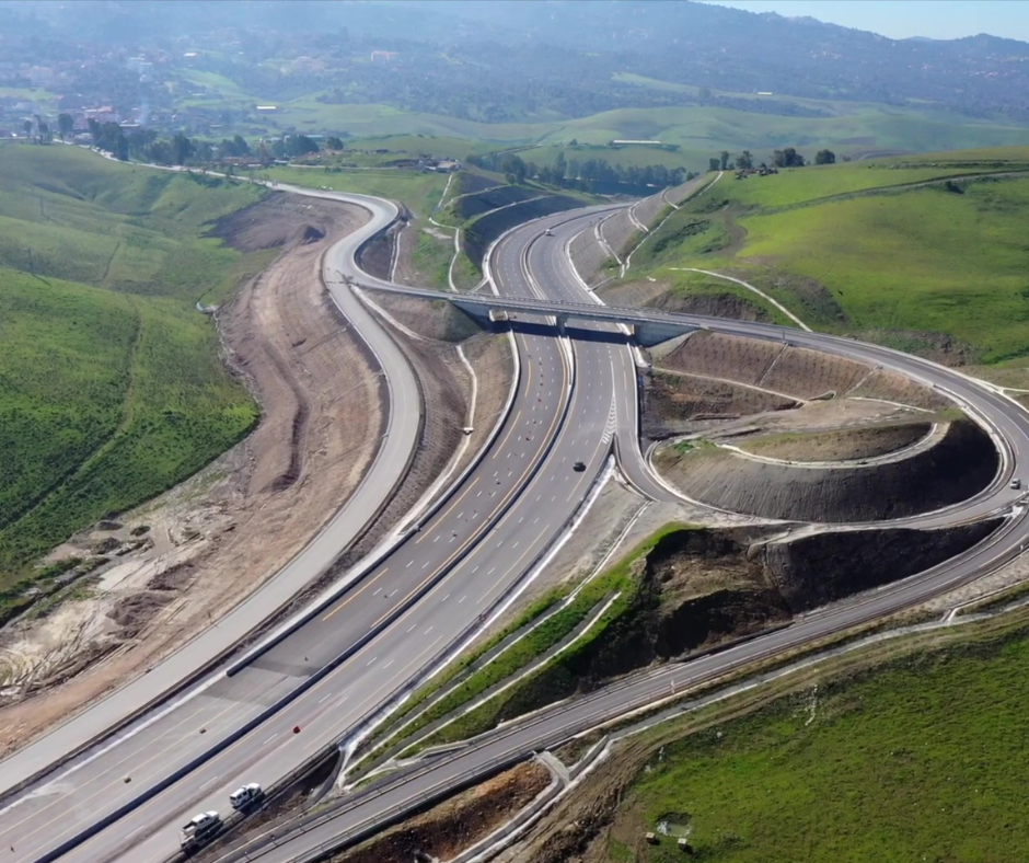 Aerial view of a modern highway interchange winding through green hills in Algeria