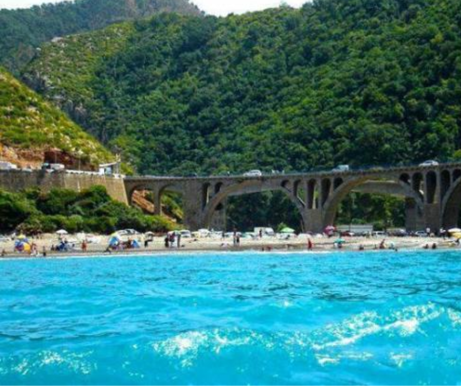 Viaduct arches above a crowded beach and turquoise water on the Jijel coast