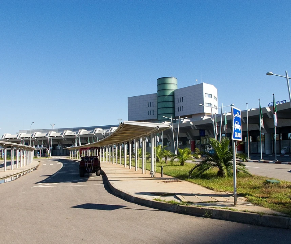 Airport terminal drop-off road lined with palms and a covered walkway