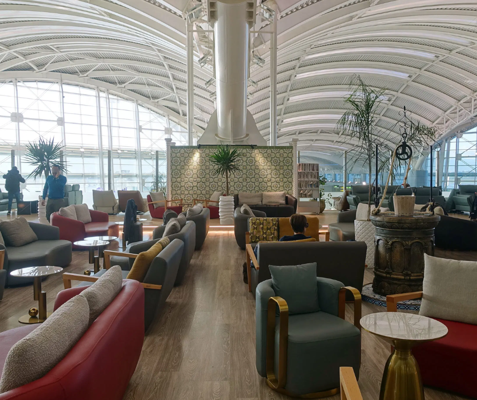 Airport premium lounge with armchairs, plants and a vaulted glass ceiling